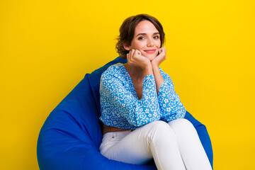 Poster - Photo of gorgeous lovely satisfied woman wear blue top sitting on bean bag keep hands under chin isolated on yellow color background