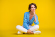© deagreez - Full size photo of optimistic gorgeous woman wear blue top white pants sit on floor hand under chin isolated on yellow color background