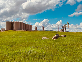 A Bakken well pad operates in the North Dakota badlands with oil tanks and a pumpjack