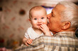 © Maryna - Elderly Man Kisses Baby Grandchild While Holding Them Indoors
