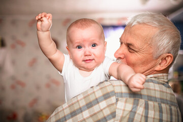 Elderly Man Holding Baby Indoors in a Plaid Shirt