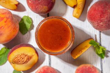 Sticker - Homemade sweet sour peach chutney jam preserves with spices and raisins, in small jar, with fresh ripe peaches on white wooden table