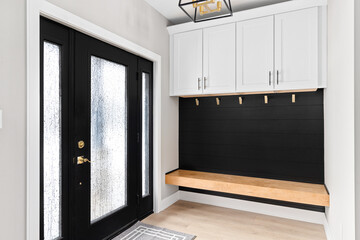 A modern farmhouse entryway with bench seating, black shiplap, white cabinets, gold coat hooks, and a black and gold light fixture,