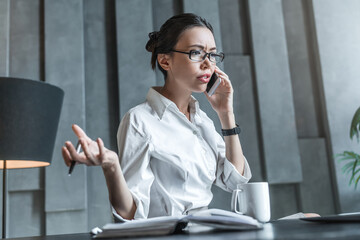 Mad businesswoman talking on phone looking at laptop. Serious concerned woman helping solving problem customer complaint, discussing business issue, having difficult conversation