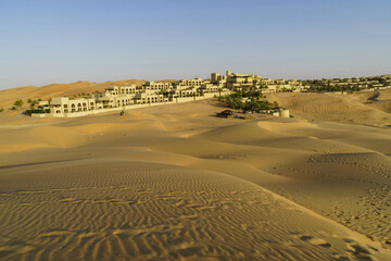 Abu Dhabi, UAE - December 2, 2014: Summer view of sand dunes on the desert against oasis resort of Qasr Al Sarab
