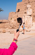© muratart - A woman's hand taking a selfie in the foreground - A beautiful young girl in shorts is standing examining historical artifacts - Ancient Temple of Karnak in Luxor - Ruined Thebes Egypt