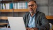 © Pinklife - A serious man with glasses and a beard works on his laptop in a stylish, book-filled office space, highlighting his intellectual demeanor and focused work approach.