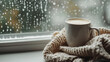© Bonsales - White cup of coffee on a knitted blanket by the window during rainy weather, cozy autumn morning concept