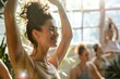 © Archibalttttt - A woman practices yoga with a smile in a group class, bathed in sunlight streaming through the window, creating a serene and positive atmosphere