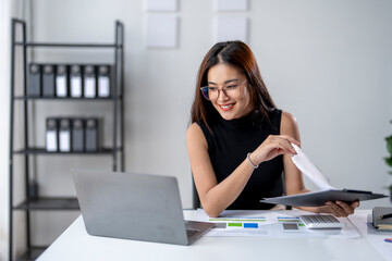 Wall Mural - A woman is sitting at a desk with a laptop and a stack of papers