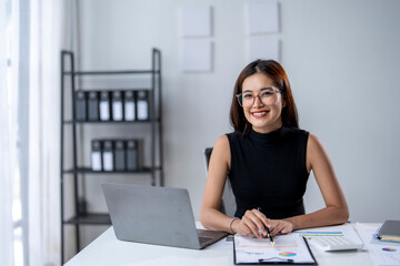 Wall Mural - A woman is sitting at a desk with a laptop and a stack of papers