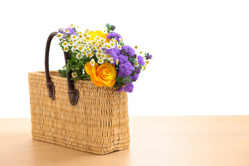 Poster - Wicker basket with beautiful flowers on light wooden table, space for text