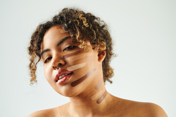 Young African American woman with foundation on face poses against vibrant backdrop.