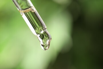 Essential oil dripping from pipette against blurred green background, closeup. Space for text