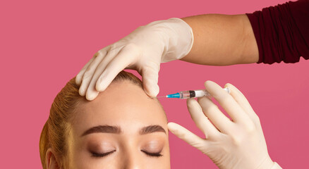 Wall Mural - A close-up image of a woman receiving an injection in her forehead from a medical professional wearing white gloves. The woman has her eyes closed and is relaxed, with her hair pulled back