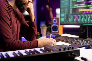 Poster - Musician composing new song in his home studio and taking notes, writing down lyrics before recording the tunes. Songwriter producing music with daw software tools and creativity.