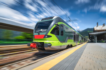 High-speed green passenger train moving at railway station platform at sunset. Train station. Modern railway transportation concept with blurred motion effect. Railroad. Commercial transport