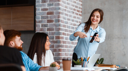 Aufkleber - A woman stands in front of a diverse group of people, presenting information using slides and gestures, showing phone. The audience members are sitting and listening attentively.