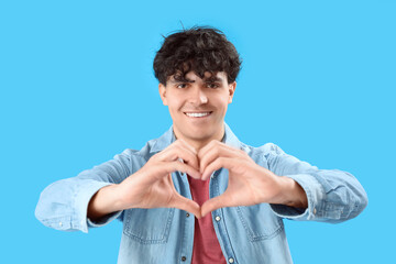 Wall Mural - Handsome young man making heart with his hands on light blue background