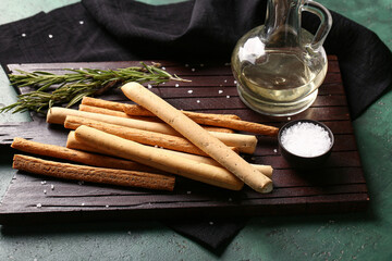 Wooden board with tasty Italian Grissini on green background