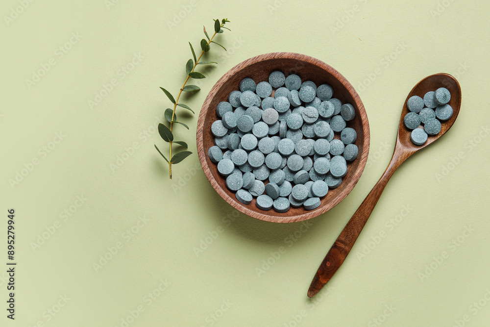 Bowl with pills, spoon and plant branch on green background