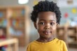 © Baba Images - Cute little boy in blurred classroom looking at camera