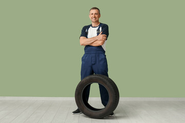 Wall Mural - Portrait of male auto mechanic with tire on green background