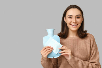 Poster - Beautiful young woman with hot water bottle and menstrual pad on grey background