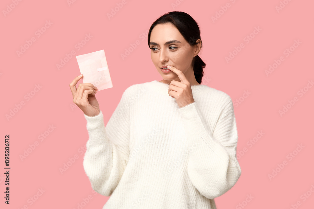 Beautiful thoughtful woman with menstrual pad on pink background