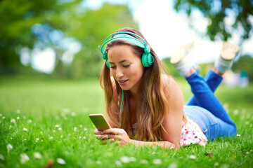 Wall Mural - Smartphone, woman and headphones on grass for music, streaming and audio book or podcast. College student, technology and happy on campus or garden for network, online and media for education in park