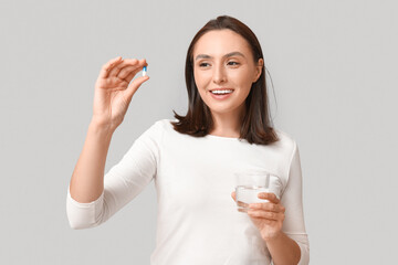 Sticker - Pretty young woman with pill and glass of water on grey background