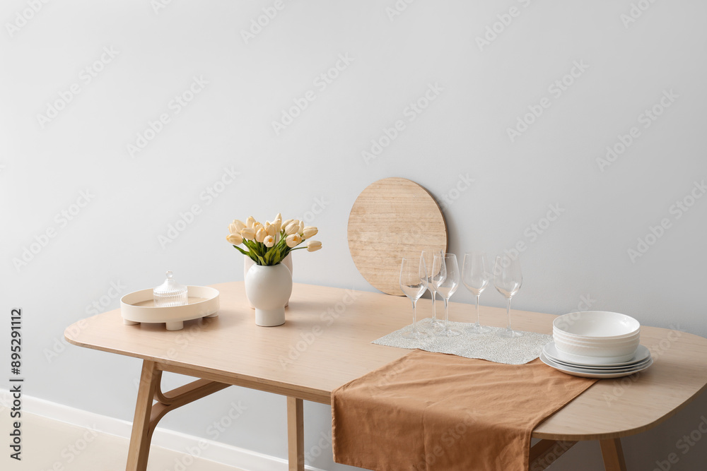 Clean tableware and tulip flowers on wooden table near light wall