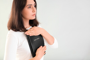 Poster - Young woman praying with Holy Bible on light background, closeup