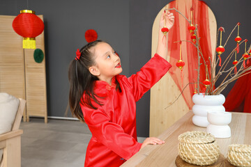 Canvas Print - Cute little Asian girl near tree branches with lanterns celebrating Chinese New Year at home