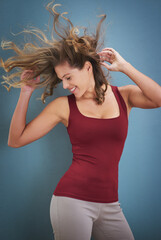 Poster - Woman, dancing and crazy hair with wind, freedom and smile from wellness and healthy in studio. Excited, carefree and confidence with hairstyle flip and blue background ready for casual dancer class