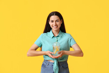 Canvas Print - Beautiful young happy woman with cup of fresh lemonade on yellow background