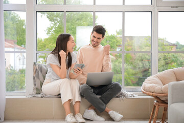 Canvas Print - Happy young couple with money and laptop at home