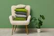 © Pixel-Shot - Stack of cushions on armchair and plant near green wall in room