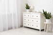 © Pixel-Shot - Stylish chest of drawers with decor and plants near white brick wall in room
