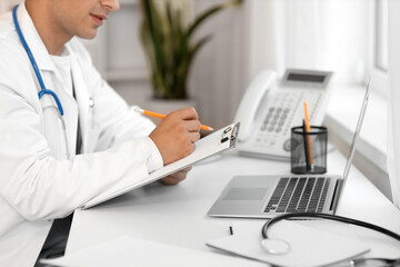 Wall Mural - Male doctor with clipboard working at table in clinic, closeup