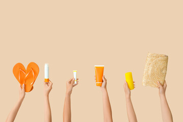 Female hands with beach accessories and bottles of sunscreen cream on beige background