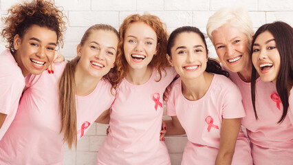 Wall Mural - Breast Cancer Survivors. Happy Diverse Ladies In T-Shirts With Pink Ribbons Hugging Standing Against White Background. Panorama