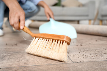 Wall Mural - Woman with brush and dustpan swiping floor under carpet at home