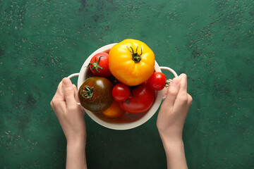 Wall Mural - Female hands with colander of different fresh tomatoes on green background