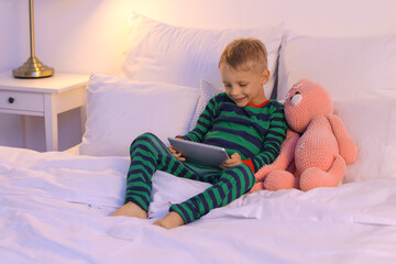 Sticker - Cute little boy watching cartoons on tablet computer in bedroom at night