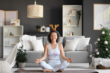 Sticker - Sporty mature woman in reindeer horns meditating at home on Christmas eve