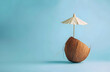 © sornram - Halved coconut with a cocktail umbrella on a blue background, evoking a tropical beach vacation and fresh summer vibes.