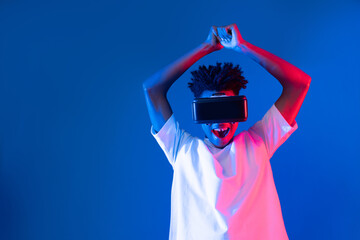 Young African American player wearing VR playing sword or baseball hologram isolated blue pink neon lighting wall connecting digital futuristic technology virtual reality metaverse world. Contrivance.