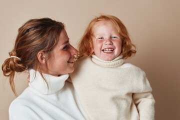 Wall Mural - Child in white turtleneck sweater held by woman with red hair in a motherly embrace