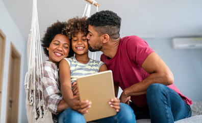 Wall Mural - Happy african family having fun with device at home. Black parents and child using digital tablet